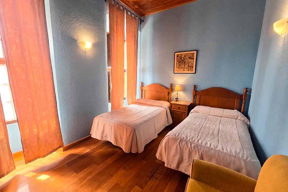 Habitación 104 Hotel Rural La Fábrica Fuente de Cantos Dormitorio con dos camas con cabecero de forja junto a un pequeño sillón.
