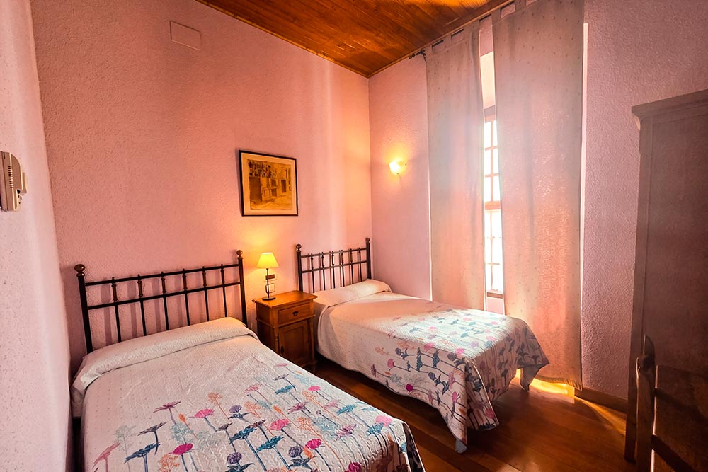 Habitación 105 Hotel Rural La Fábrica Fuente de Cantos Dormitorio con dos camas con cabecero de forja junto a un pequeño sillón.