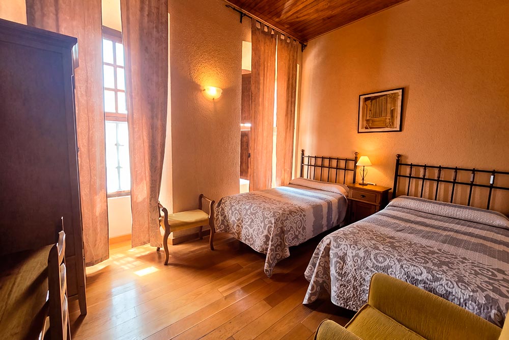 Habitación 107 Hotel Rural La Fábrica Fuente de Cantos Dormitorio con dos camas con techo abuhardillado de madera.