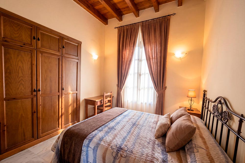 Habitación 109 Hotel Rural La Fábrica Fuente de Cantos Dormitorio con dos camas con cabecero de forja, suelo y techo de madera.