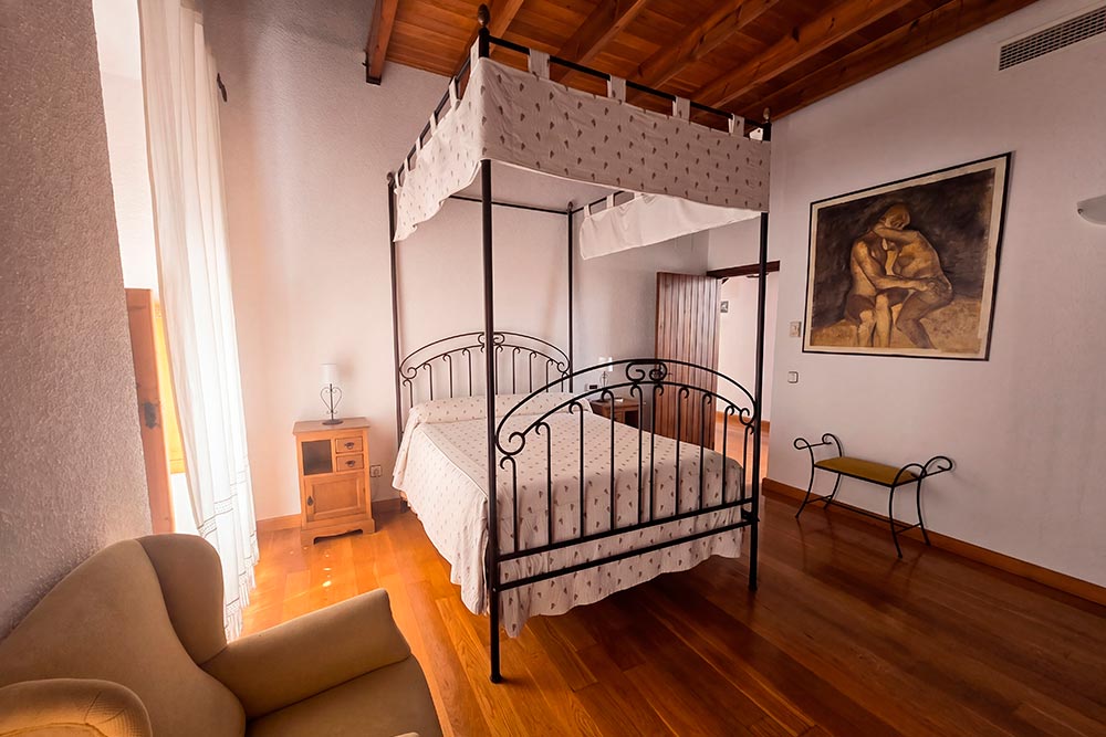 Habitación 207 Hotel Rural La Fábrica Fuente de Cantos Dormitorio con dos camas con cabecero de forja, suelo y techo de madera.