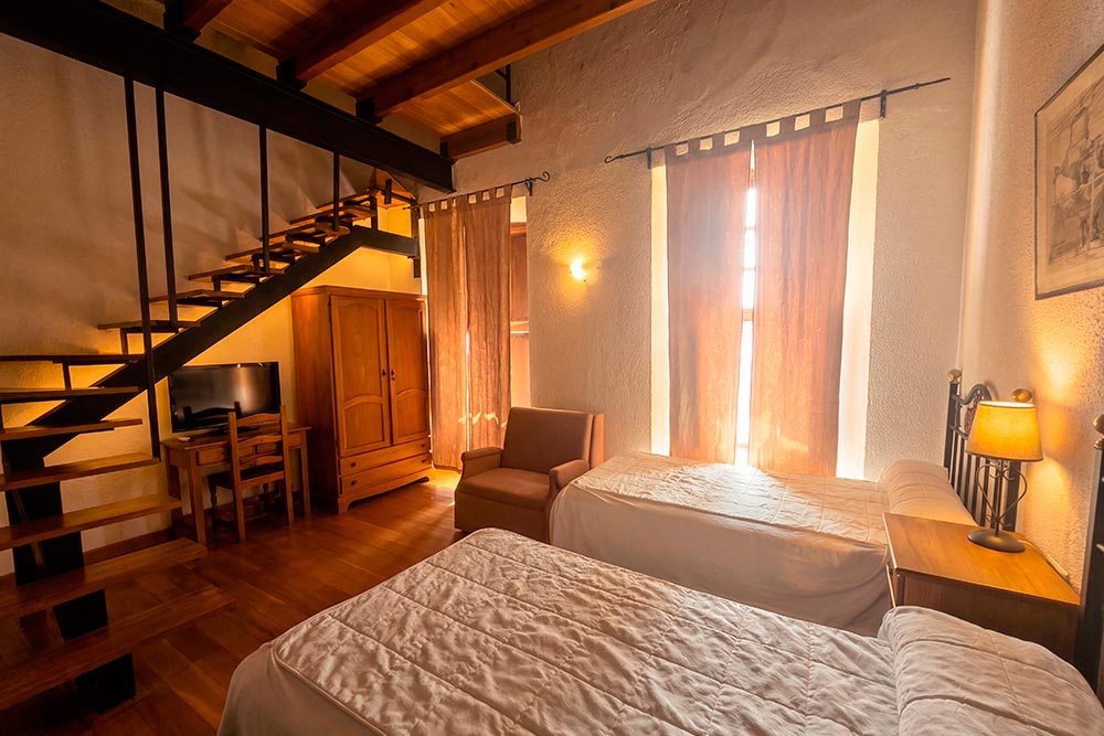 Habitación 106 Hotel Rural La Fábrica Fuente de Cantos Un acogedor dormitorio con una cama con dosel y una mesilla con un jarrón con rosas.